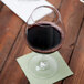 A Carlisle plastic balloon wine glass filled with red wine on a table with a napkin.