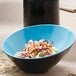 A blue and black GET Brasilia melamine bowl with food on a table.