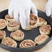 A hand in a glove holding a cinnamon roll and placing it in a Chicago Metallic BAKALON deep dish pizza pan.