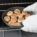 A person in gloves holding a Chicago Metallic BAKALON deep dish pizza pan with cinnamon rolls.