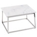 A Tablecraft stainless steel tall half size reversible riser on a white table with metal legs.