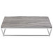 A Tablecraft stainless steel short full size reversible riser on a grey rectangular table with metal legs.