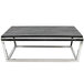 A stainless steel Tablecraft short half size reversible riser on a black table with metal legs.