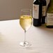 A customizable Arcoroc wine glass filled with white wine on a table.