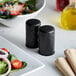 American Metalcraft black hammered finish salt and pepper shakers on a table with a salad.