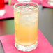 A Libbey highball glass of orange liquid with ice and a slice of lemon on a pink napkin.