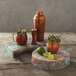 An American Metalcraft faux reclaimed wood rectangular melamine riser with rustic copper mule tumblers and a lime wedge on a wooden surface.
