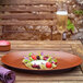 A RAK Porcelain Neo Fusion Terra Brown plate with food, fruit, and flowers on a table.