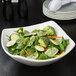 A white square stoneware bowl filled with salad and vegetables.