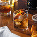 A glass of whiskey with ice, orange slices, and cinnamon sticks.
