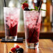 Two glasses of Monin wildberry drinks with ice, straws, and berries on a wooden table.