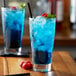 A glass of Monin Blue Raspberry Syrup with blue liquid, ice, and raspberries.
