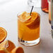 A glass of orange juice with Monin Premium Orange Tangerine Flavoring Syrup and a slice of orange.