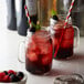 A mason jar filled with a red drink and a straw with a blackberry on it.