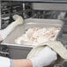 A person in gloves holding a Choice stainless steel steam table pan of meat.