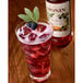 A glass of Monin blackberry sangria mix with ice and blackberries on a table.