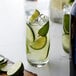 A glass of cucumber and mint drink with lime slices on a table with a bottle of Monin Premium Cucumber Flavoring Syrup.
