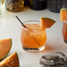 A glass of Monin cantaloupe-flavored drink with a slice of melon on the rim and a straw.