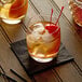 A glass of whiskey with Monin Premium Hickory Smoke Flavoring Syrup and ice with a cherry on top.