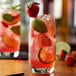 A glass of pink strawberry and lime drink with strawberries and limes.