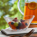 A Libbey Tritan plastic bowl filled with fruit on a table with a pitcher of liquid.