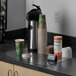 A clear ES Robbins vinyl countertop mat on a counter with coffee cups and a container.