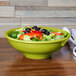 A green Fiesta pedestal serving bowl filled with salad on a table.