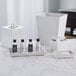A white melamine square tissue box cover on a table with other white hotel bathroom accessories.