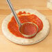 A spoon spreading sauce onto pizza dough in a pizza pan.