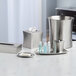A brushed stainless steel container with a lid holding small bottles of toiletries.