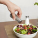 A hand using a Thunder Group Mushroom Top Paneled Salt Shaker to sprinkle salt on a bowl of salad.