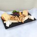 A black GET Melamine tray with cheese, grapes, and crackers on a table.