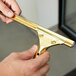 A close-up of a hand holding a Unger GoldenClip window squeegee with a brass handle.