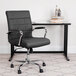 A Flash Furniture black vinyl office chair with chrome legs and armrests next to a black desk.