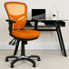 A Flash Furniture orange mesh office chair next to a black desk.