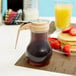 A Tablecraft polypropylene syrup dispenser with a brown liquid and a stack of pancakes with strawberries.