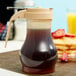 A Tablecraft syrup dispenser filled with brown syrup on a table with pancakes.