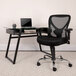 A Flash Furniture black mesh office chair next to a glass desk with a laptop on it.