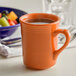 A Tuxton papaya gala mug filled with coffee on a table in front of a bowl of fruit.