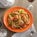 A Tuxton Concentrix papaya china plate with shrimp pasta and basil on it with a fork.