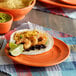A Tuxton Concentrix papaya plate with shrimp tacos, black beans, and cheese on a table.