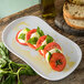 A Carlisle Griege melamine platter with tomatoes, basil, and bread on a table.