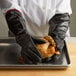 A person wearing Essentialware black neoprene gloves holding a chicken on a tray.