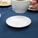 A hand holding a Tuxton bright white Alaska saucer with a cup of coffee on it.