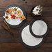 A white marble and black slate melamine serving platter with food and a bowl of yellow liquid on a wooden surface.