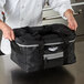 A chef holding a large black Vollrath 3-Series insulated food pan carrier bag.