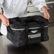A chef holding a Vollrath medium black insulated food pan carrier bag.