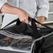 A chef holding a black and silver Vollrath insulated pizza delivery bag with a black strap.