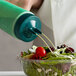 A person using a Vollrath Vista Green Twin Tip Squeeze Bottle to pour white dressing onto a salad.