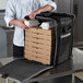 A chef putting pizza boxes in a large Vollrath insulated tower bag.